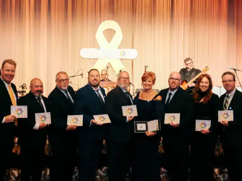 1. Group of people at Camp One Step fundraising event with ribbon symbol in background.