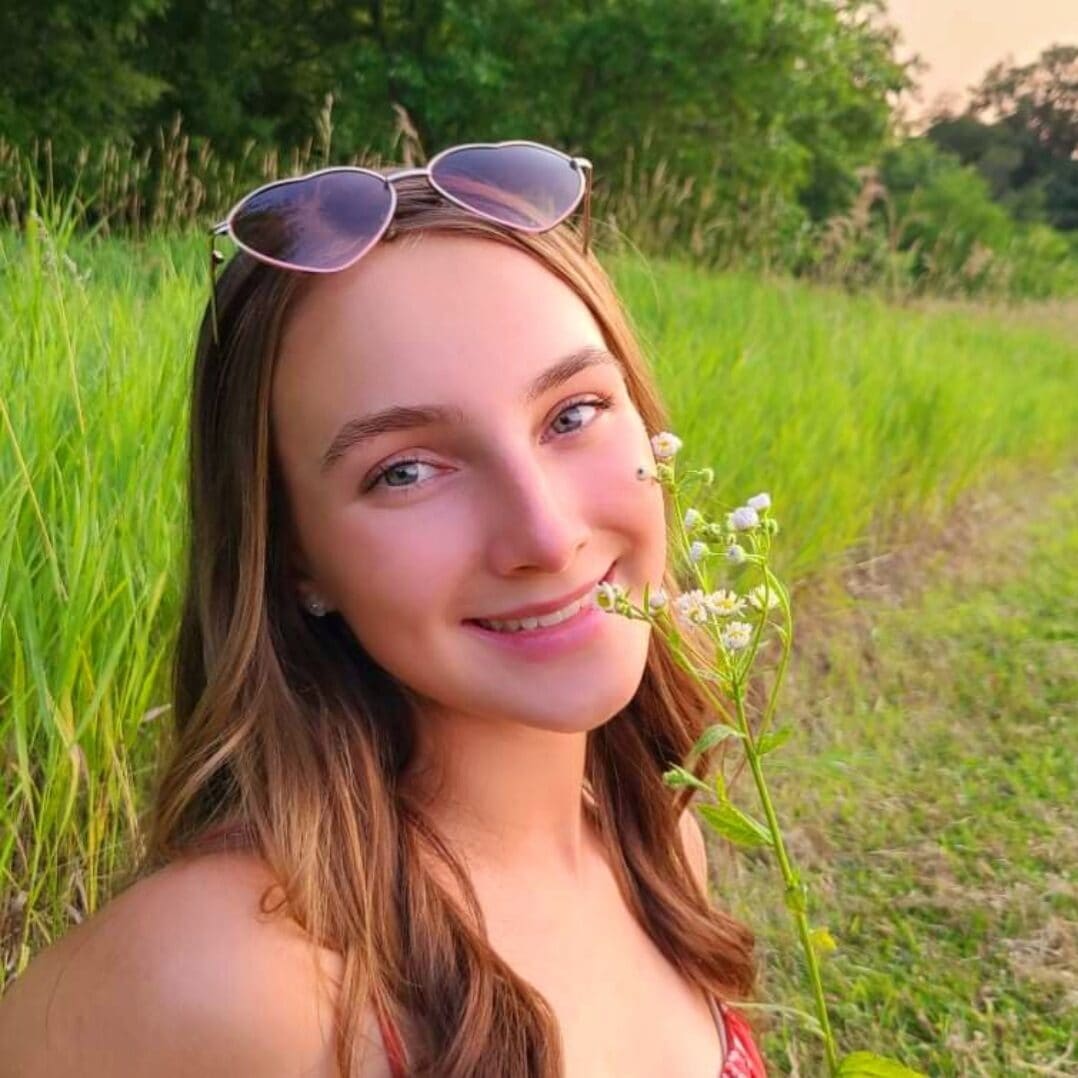 Bright young woman smiling in a grassy field, enjoying nature at Camp One Step outdoor camp experience.