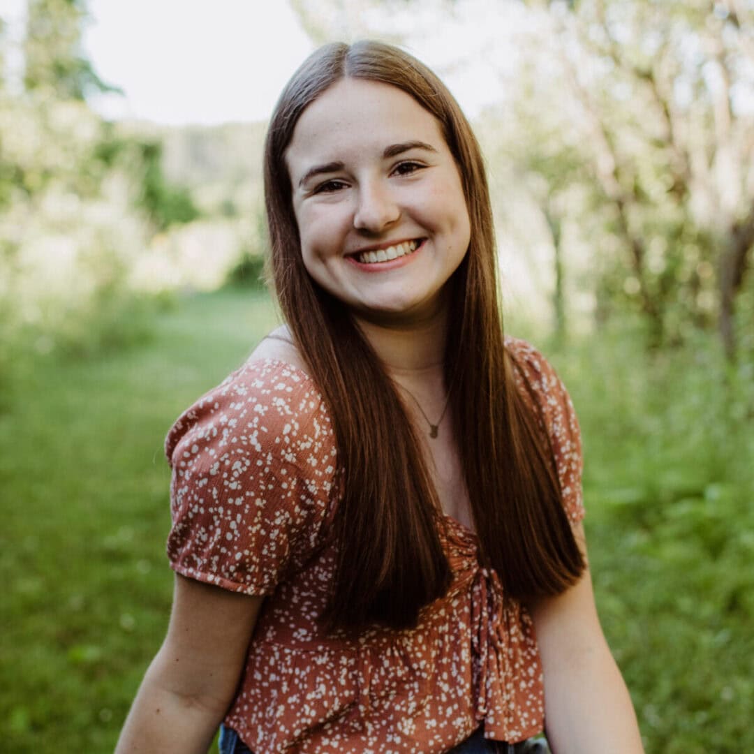 Bright young woman smiling outdoors at Camp One Step, surrounded by nature.