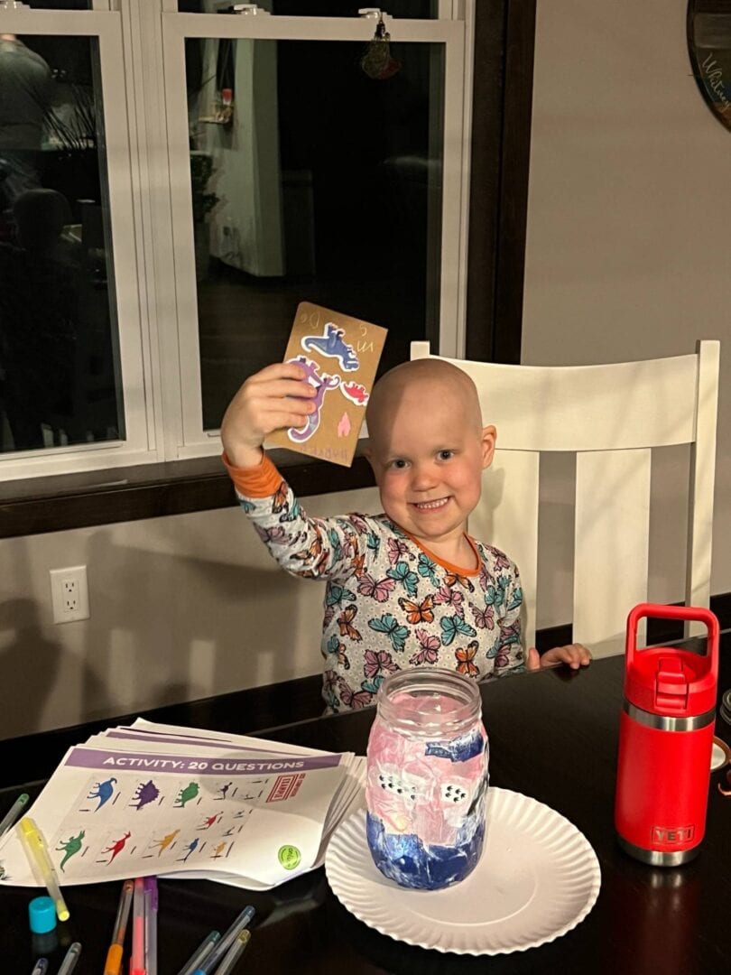 Adorable young girl smiling, holding a colorful craft project at Camp One Step.
