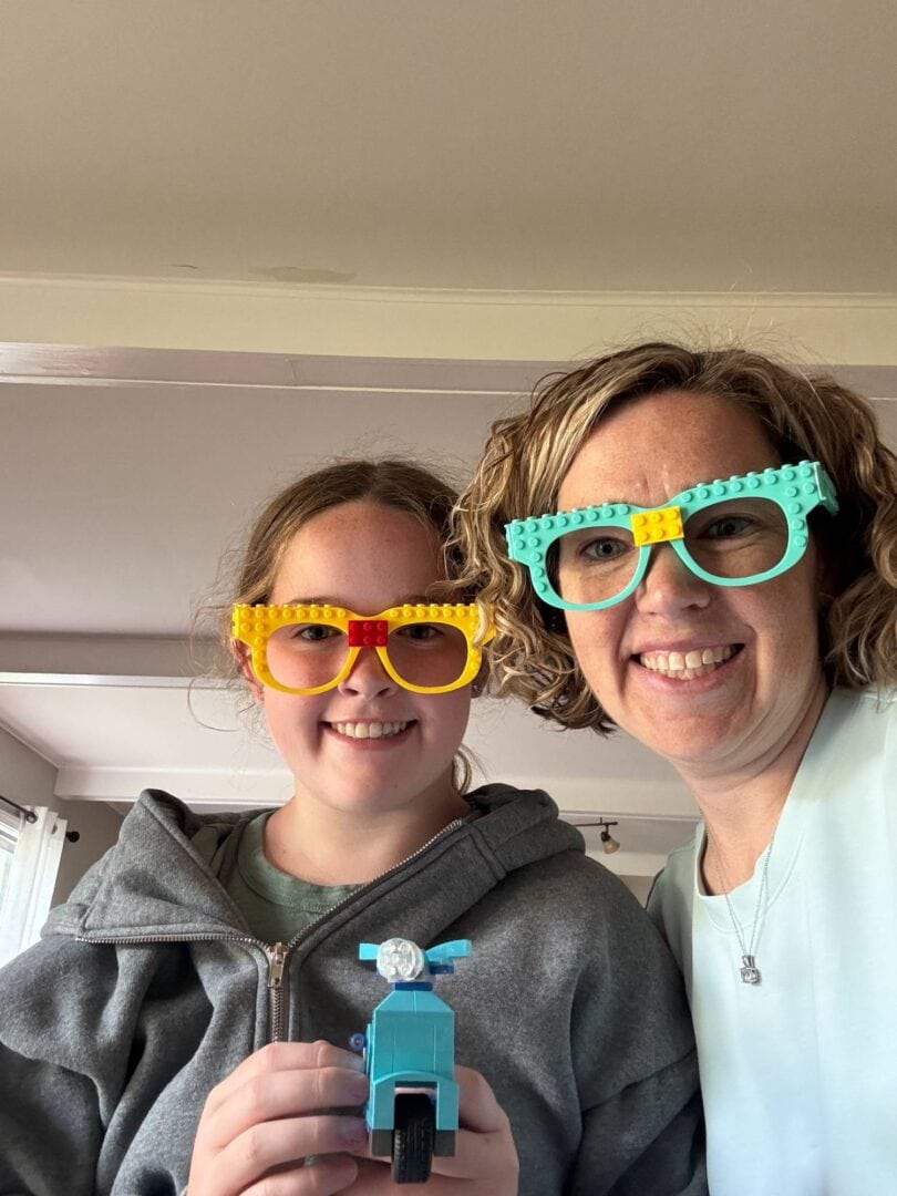 Bright blue and yellow Lego glasses worn by smiling woman and girl indoors.