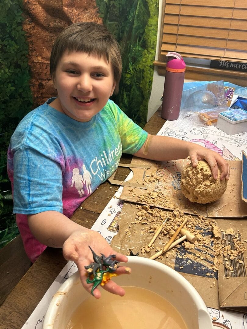 Young boy making arts and crafts at camp with modeling clay and small figurines.