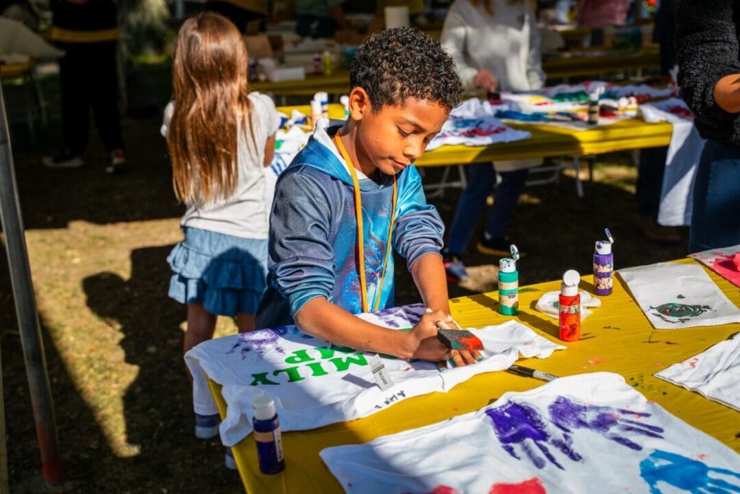 Colorful kids painting T-shirts at Camp One Step outdoor activity.