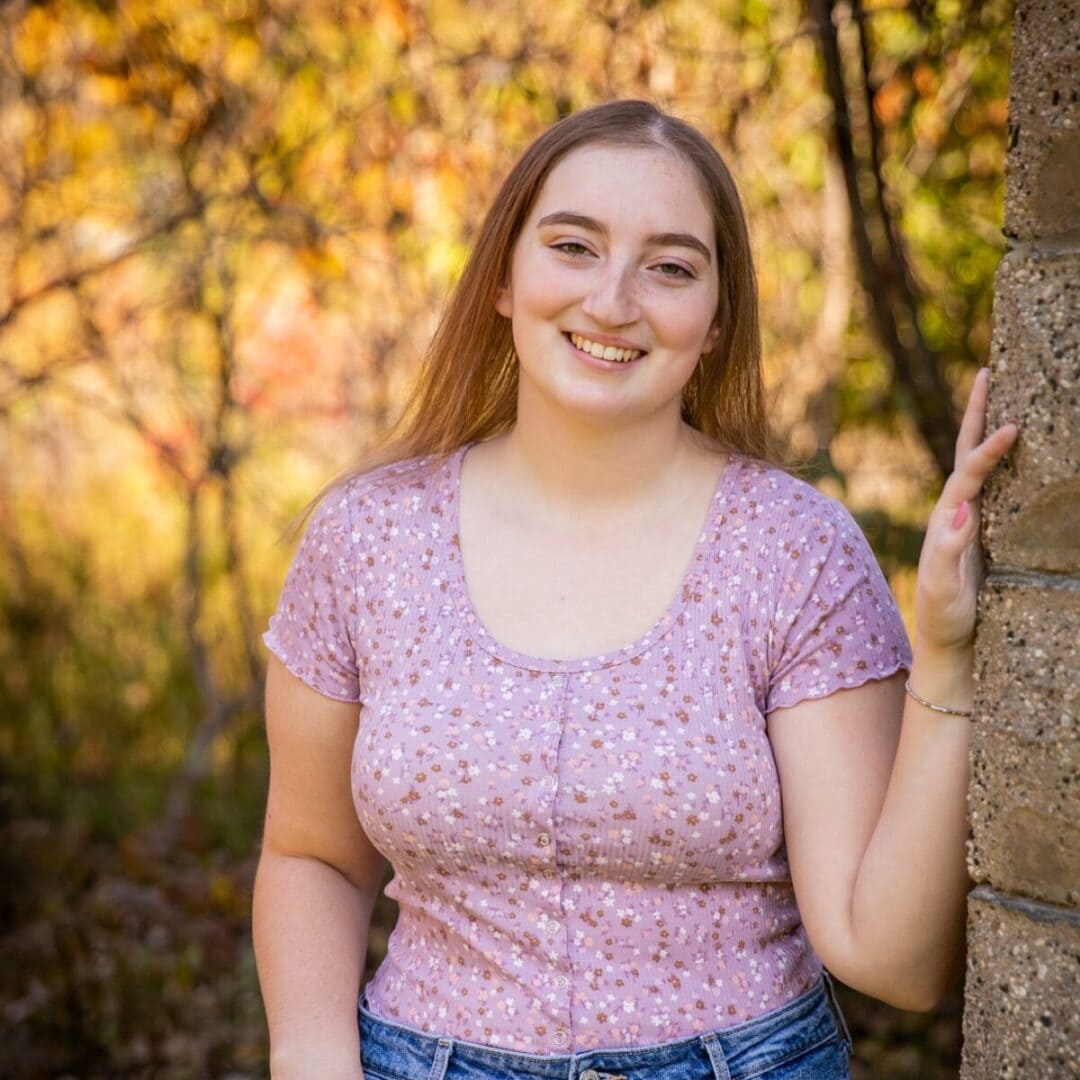 Youthful woman with long brown hair smiling outdoors in autumn setting at Camp One Step.