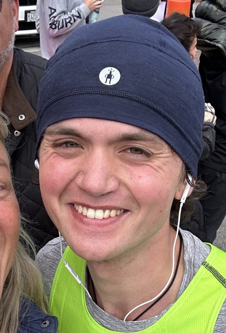 Smiling young man wearing a blue beanie and neon yellow vest at Camp One Step outdoor event.