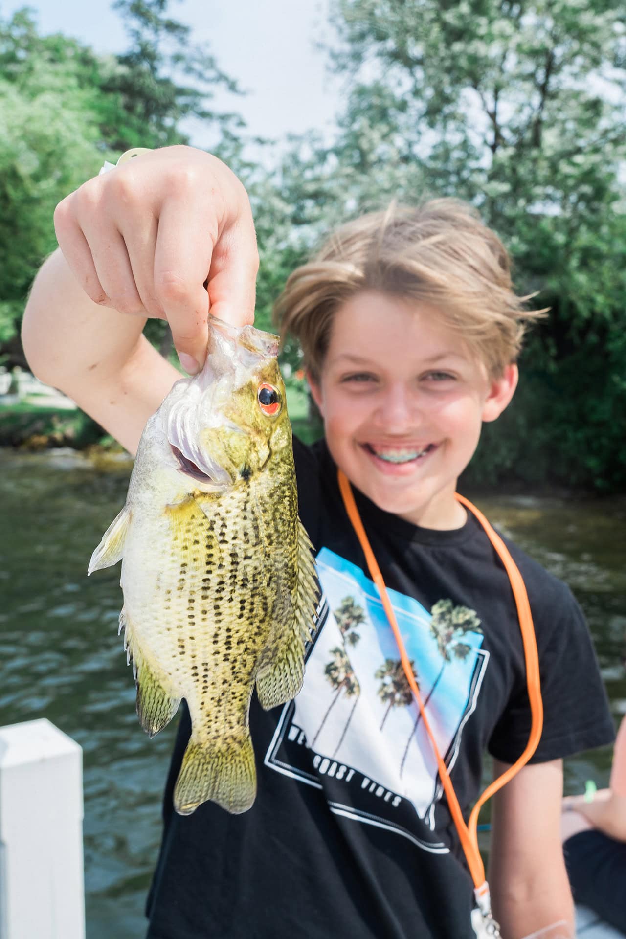 Bright young camper holding a freshly caught fish at Camp One Step outdoor adventure camp.