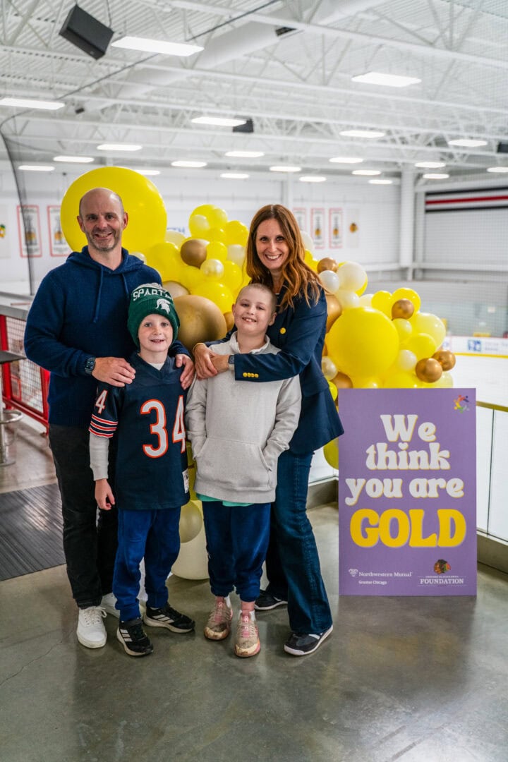 Family celebrating at ice rink with yellow balloon decorations for charity event.