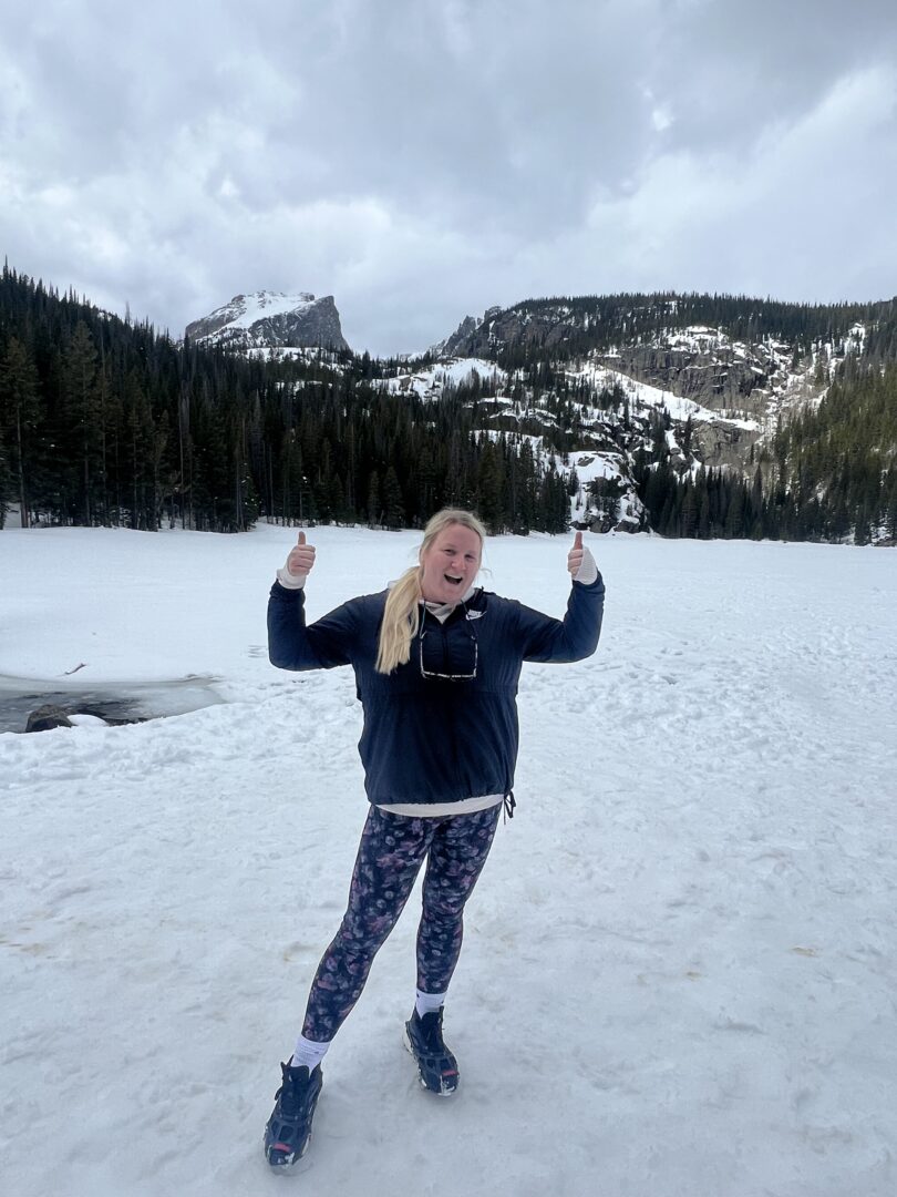 A woman happily enjoying outdoor activities at Camp One Step, surrounded by snow-covered mountains and trees, winter scenery.