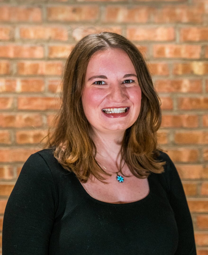 Smiling woman outdoors at Camp One Step, surrounded by a brick wall.