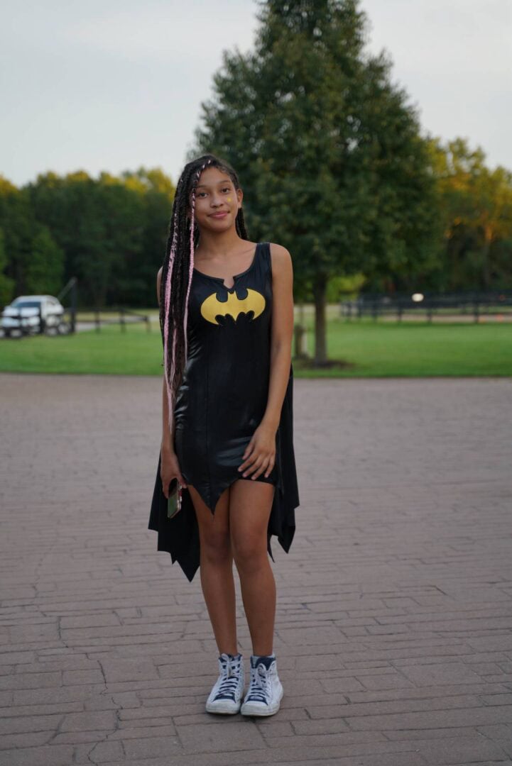 Girl in Batman-themed dress at Camp One Step outdoor camp setting.