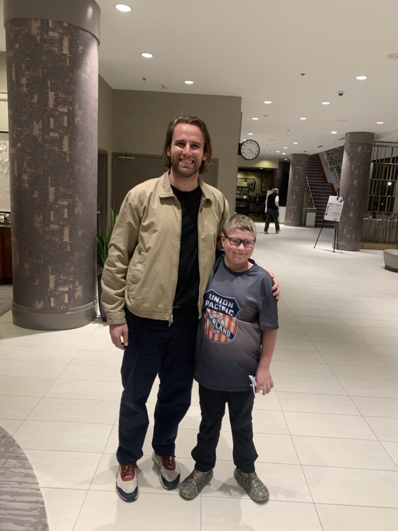 1. Happy man and boy at Camp One Step charity event, smiling inside a modern hotel lobby.
