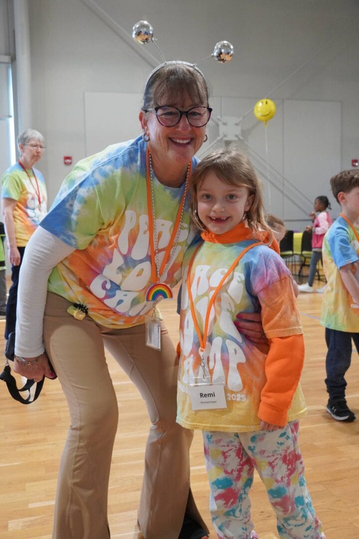 Smiling woman and girl at Camp One Step event, both wearing rainbow tie-dye shirts and medals.