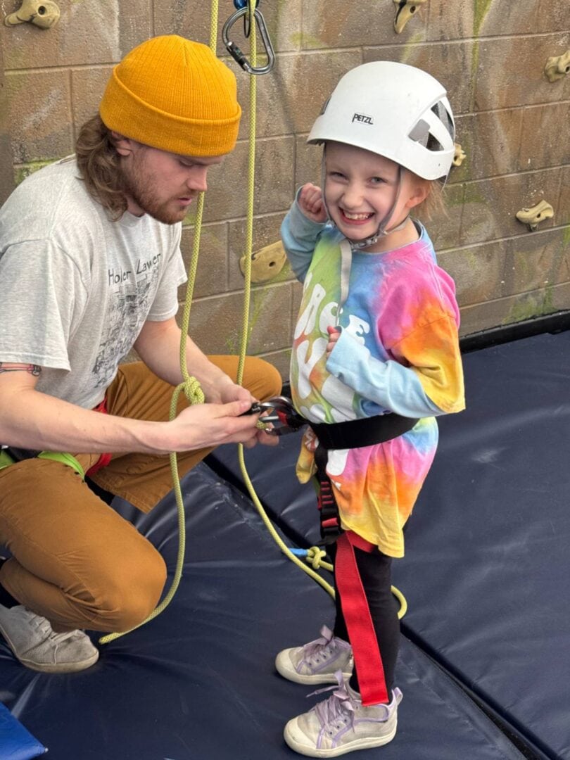 Young girl with harness and helmet smiling during rock climbing activity at Camp One Step.