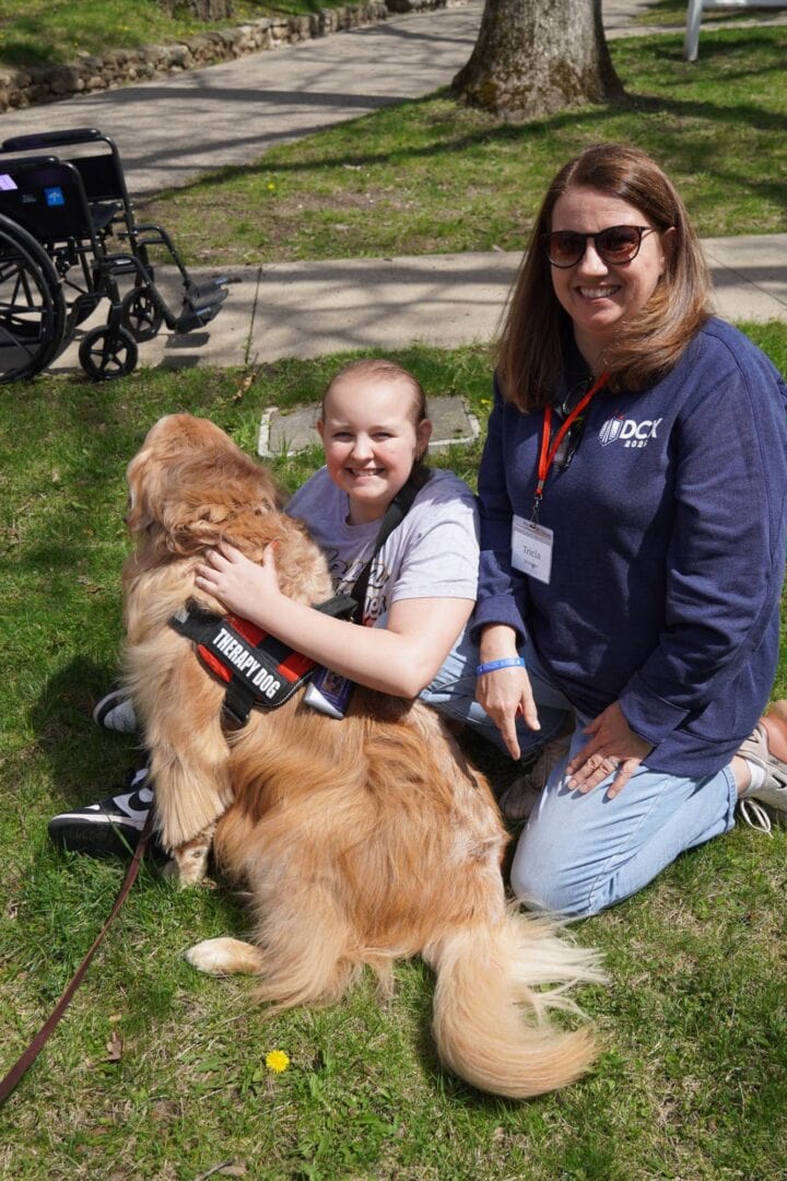 Therapy dog at Camp One Step with smiling girl and caregiver outdoors.