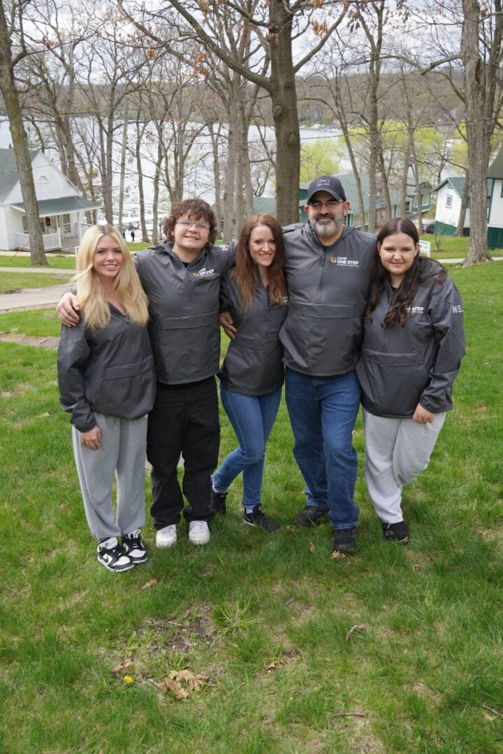 Family group wearing Camp One Step jackets outdoors at a scenic park.