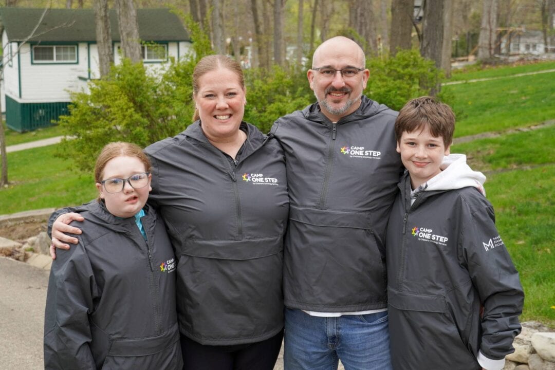 Supportive family at Camp One Step, a children's oncology charity, enjoying outdoor activities in personalized jackets.