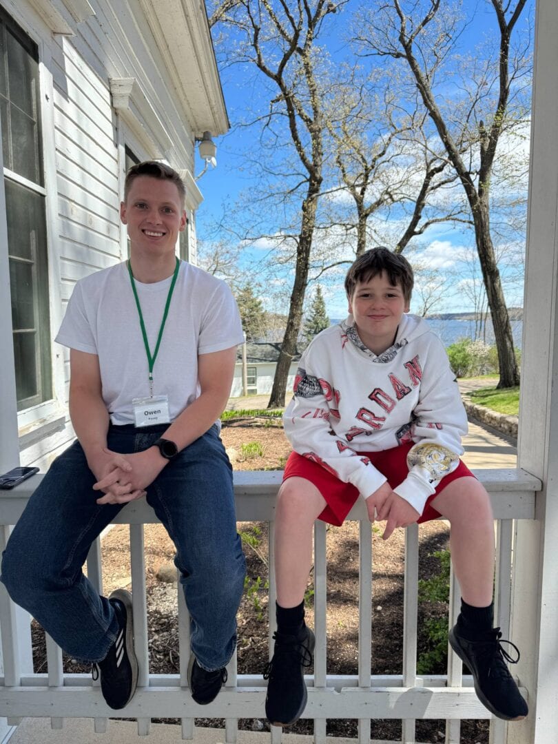 Owen and a young camper sitting on a porch railing at Camp One Step, enjoying outdoor activities in spring.