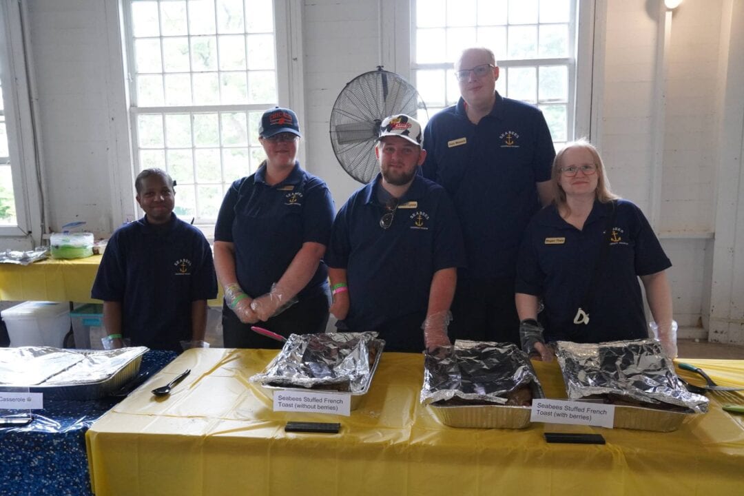 Volunteers at Camp One Step serve food, dressed in navy uniforms, with a cheerful group atmosphere.
