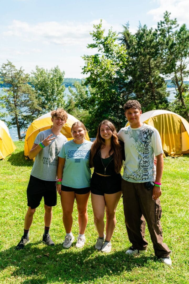 Young people smiling and enjoying their time at Camp One Step with yellow tents and nature backdrop.