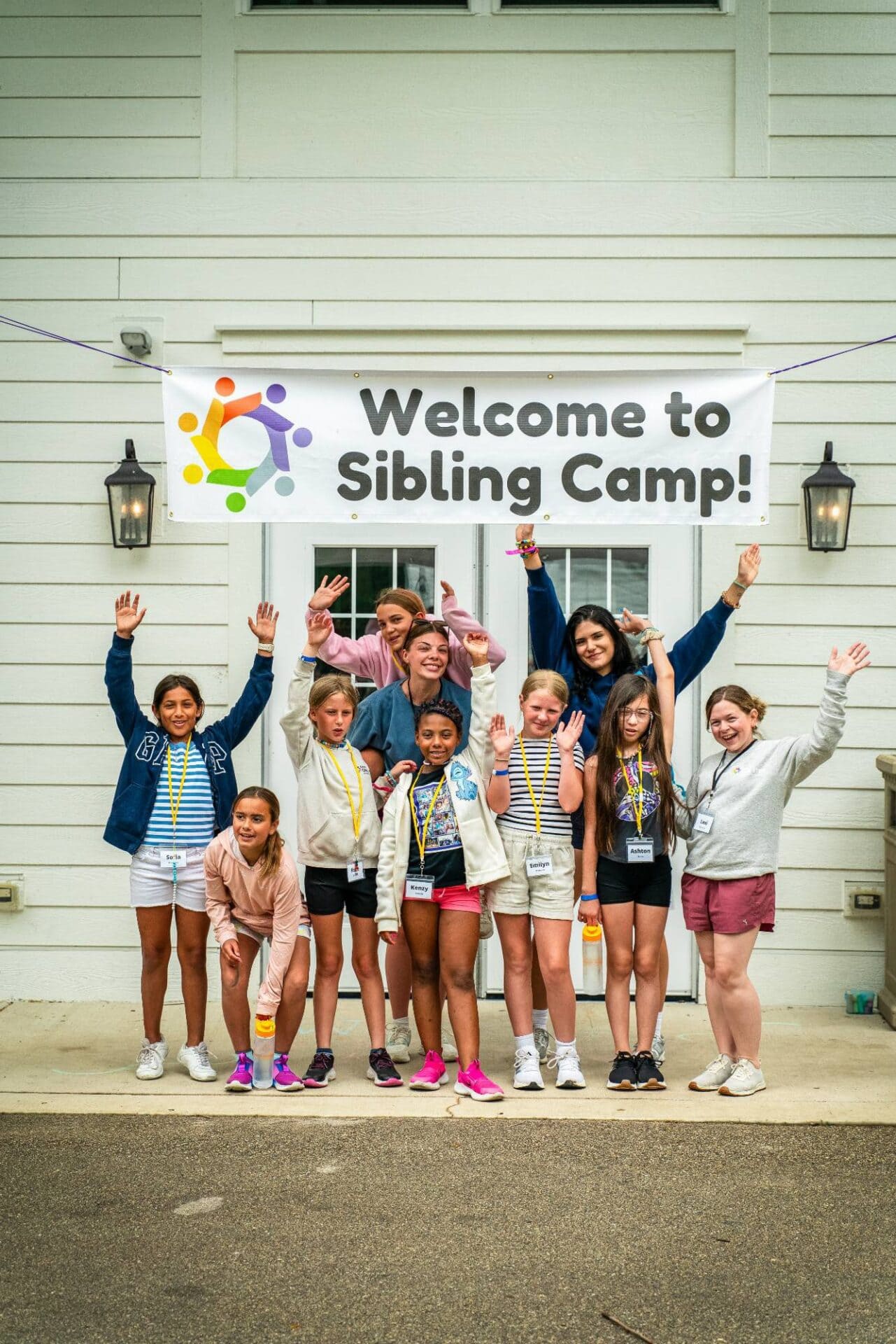Children smiling at sibling camp event, diverse group celebrating together outside building.