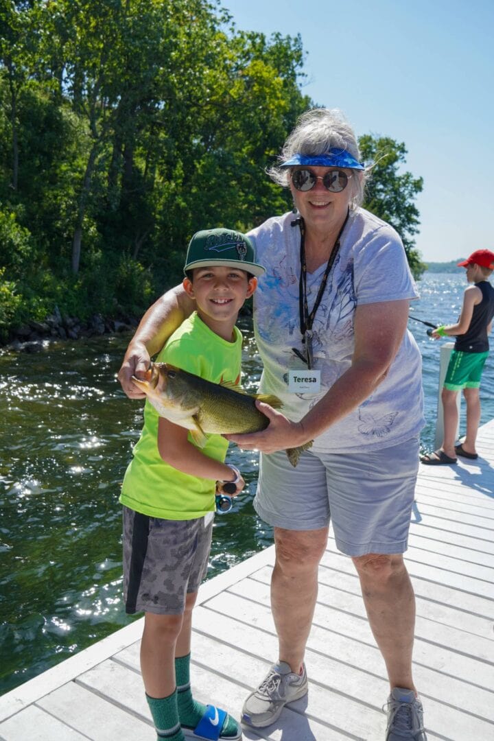 Smiling boy and woman holding a caught fish at Lake Camp One Step, summer camp fishing activity.