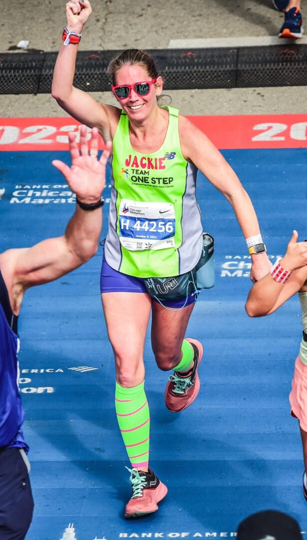 High-energy marathon runner smiling at Chicago Marathon finish line, promoting fitness and cancer awareness.
