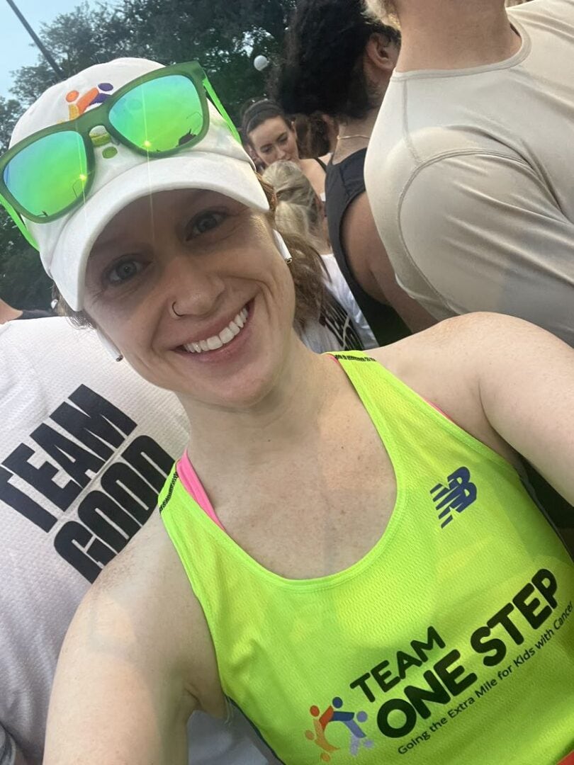 Smiling woman in bright yellow running tank top with "Team One Step" logo, surrounded by fellow runners.
