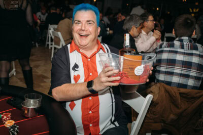 Smiling man serving drinks at Camp One Step fundraising event, lively party atmosphere.