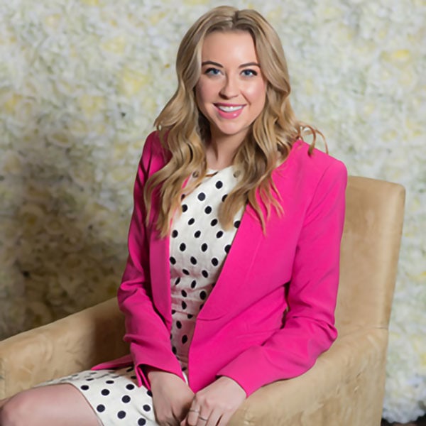 1. Young woman in pink blazer and polka dot dress sitting on beige armchair.