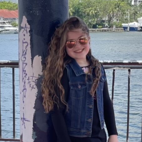 Smiling girl with sunglasses at Camp One Step by the water, outdoor youth camp in a scenic setting.