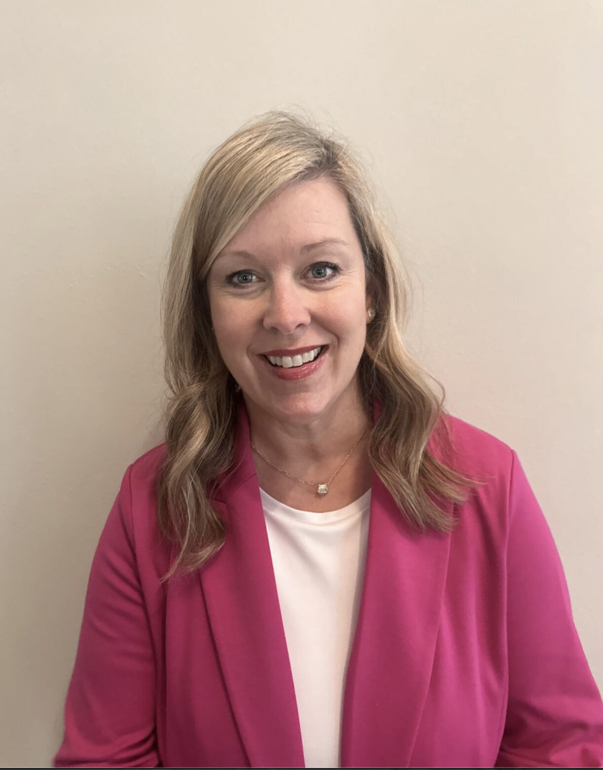 Smiling woman in pink blazer against neutral wall