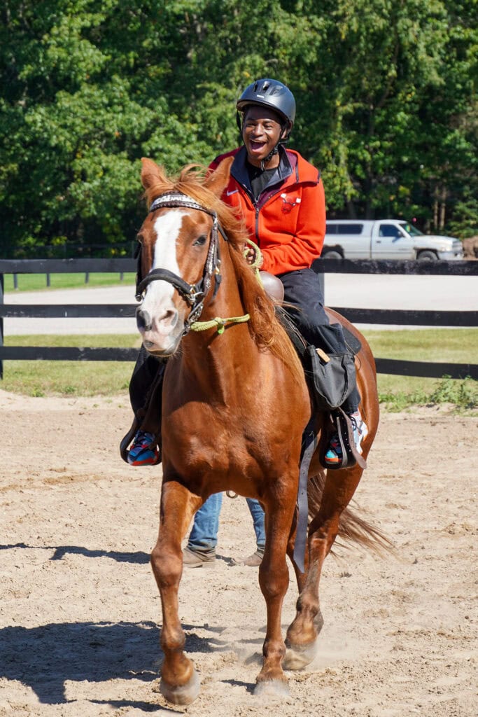 Happy person riding a horse at Camp One Step outdoor activity.