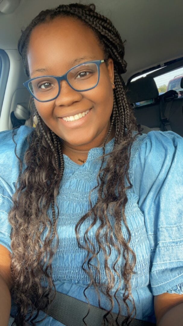 Bright smiling woman wearing glasses, sitting in a car for outdoor camping at Camp One Step.