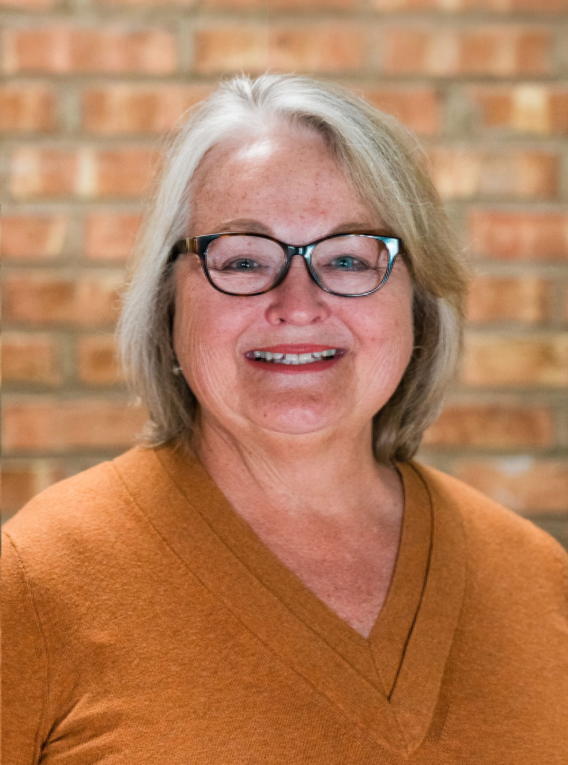 Warm, welcoming woman with glasses at Camp One Step healing retreat.
