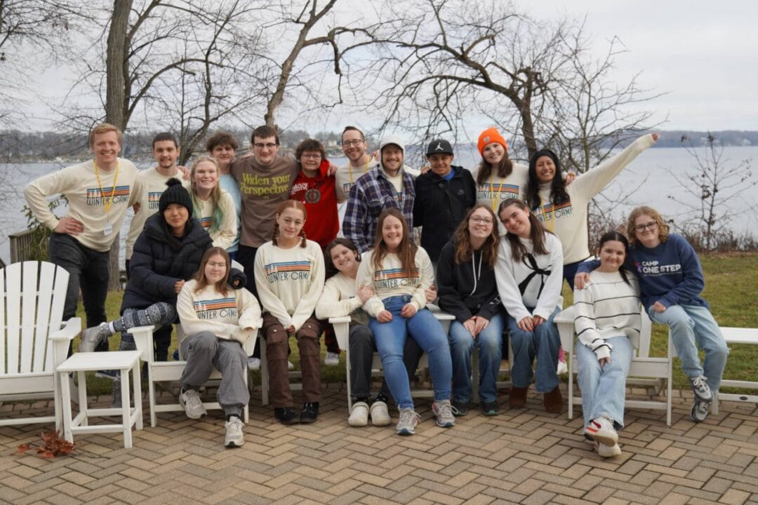 Fun group photo at Camp One Step winter camp by the lake, featuring smiling campers and staff in cozy outdoor attire.