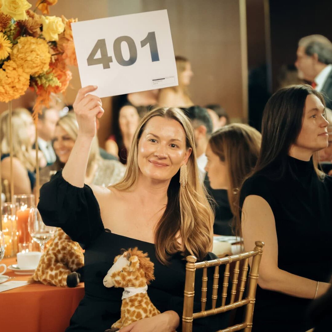 Happy woman holding up a table number at Camp One Step charity event with floral decor.