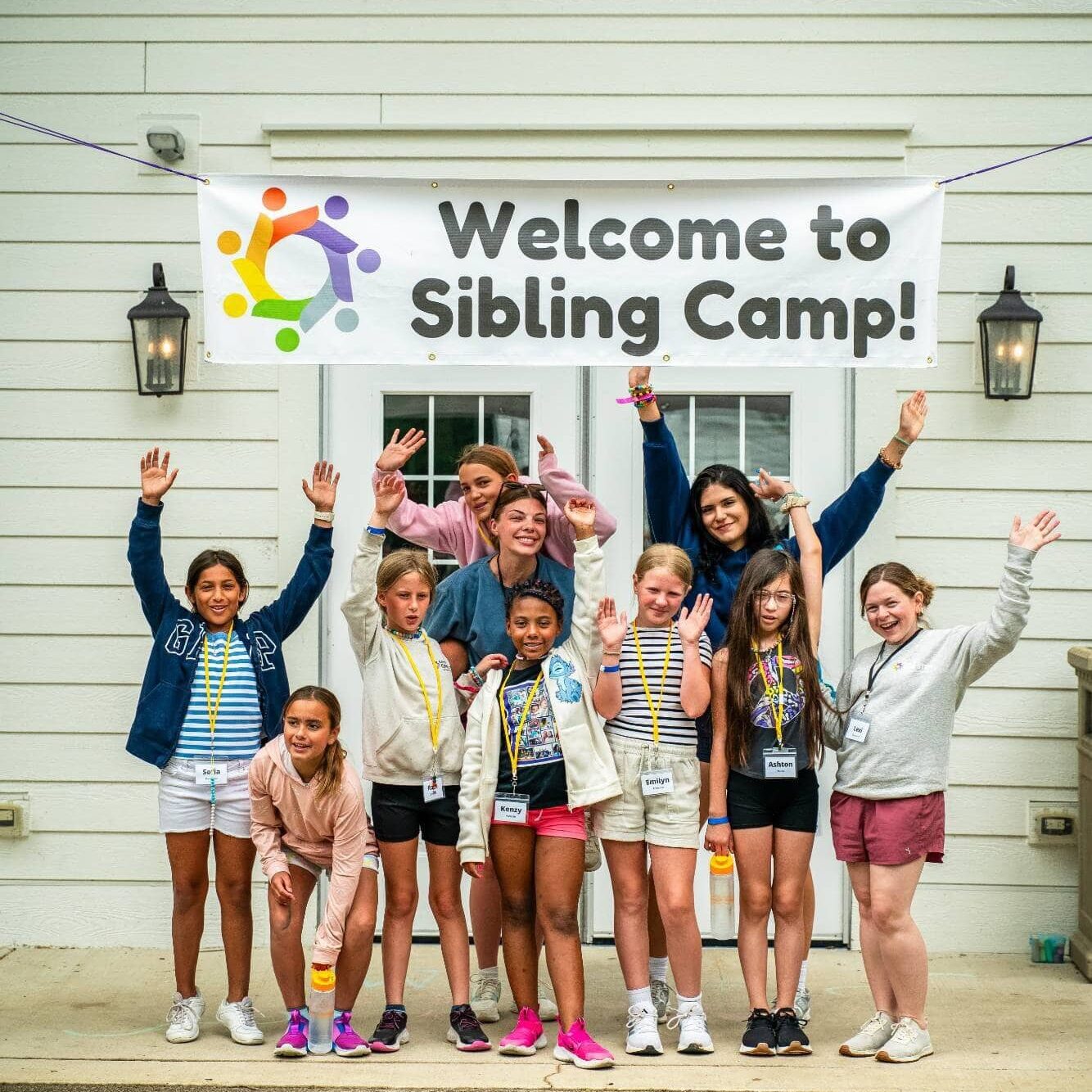 Children smiling at sibling camp event, diverse group celebrating together outside building.