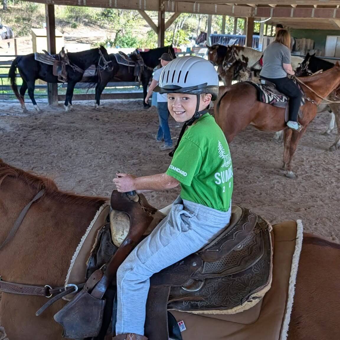 Young rider enjoying horse riding experience with safety gear.