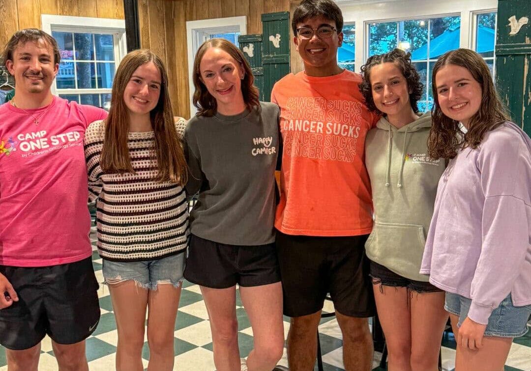 Young campers at Camp One Step cancer support program, smiling in a cozy indoor setting with wooden walls.