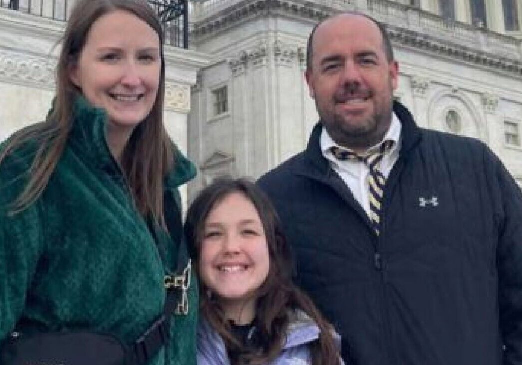 Family smiling outdoors in front of a historic building, representing community and adventure at Camp One Step.