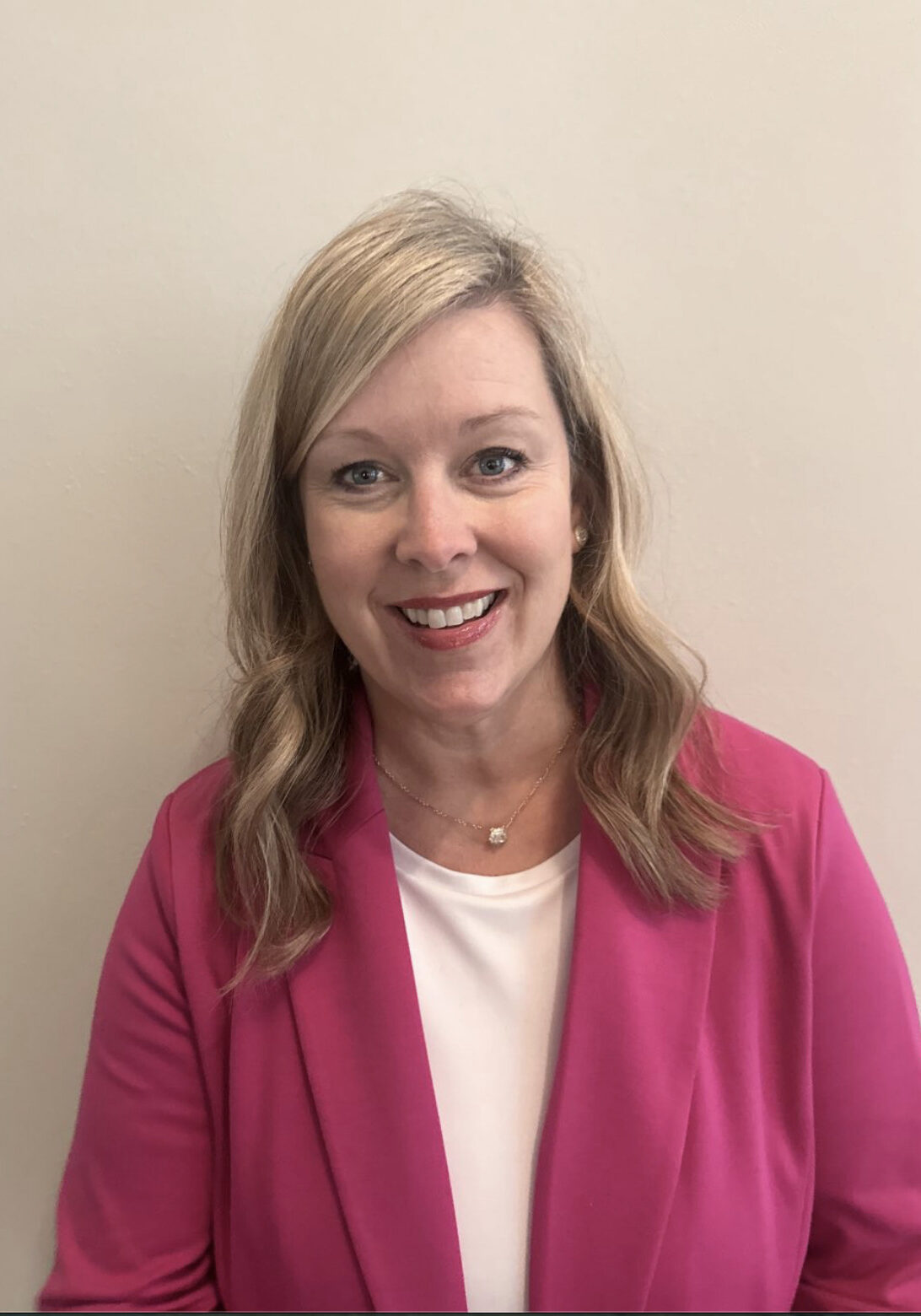 Smiling woman in pink blazer against neutral background