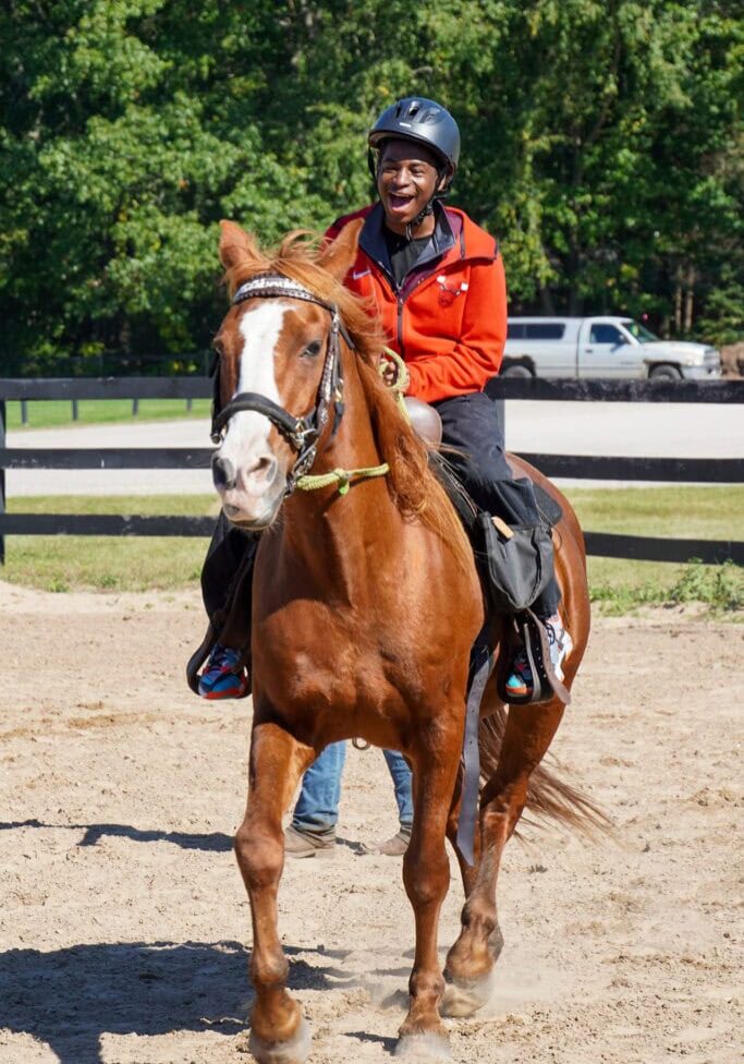 Happy person riding a horse at Camp One Step outdoor activity.