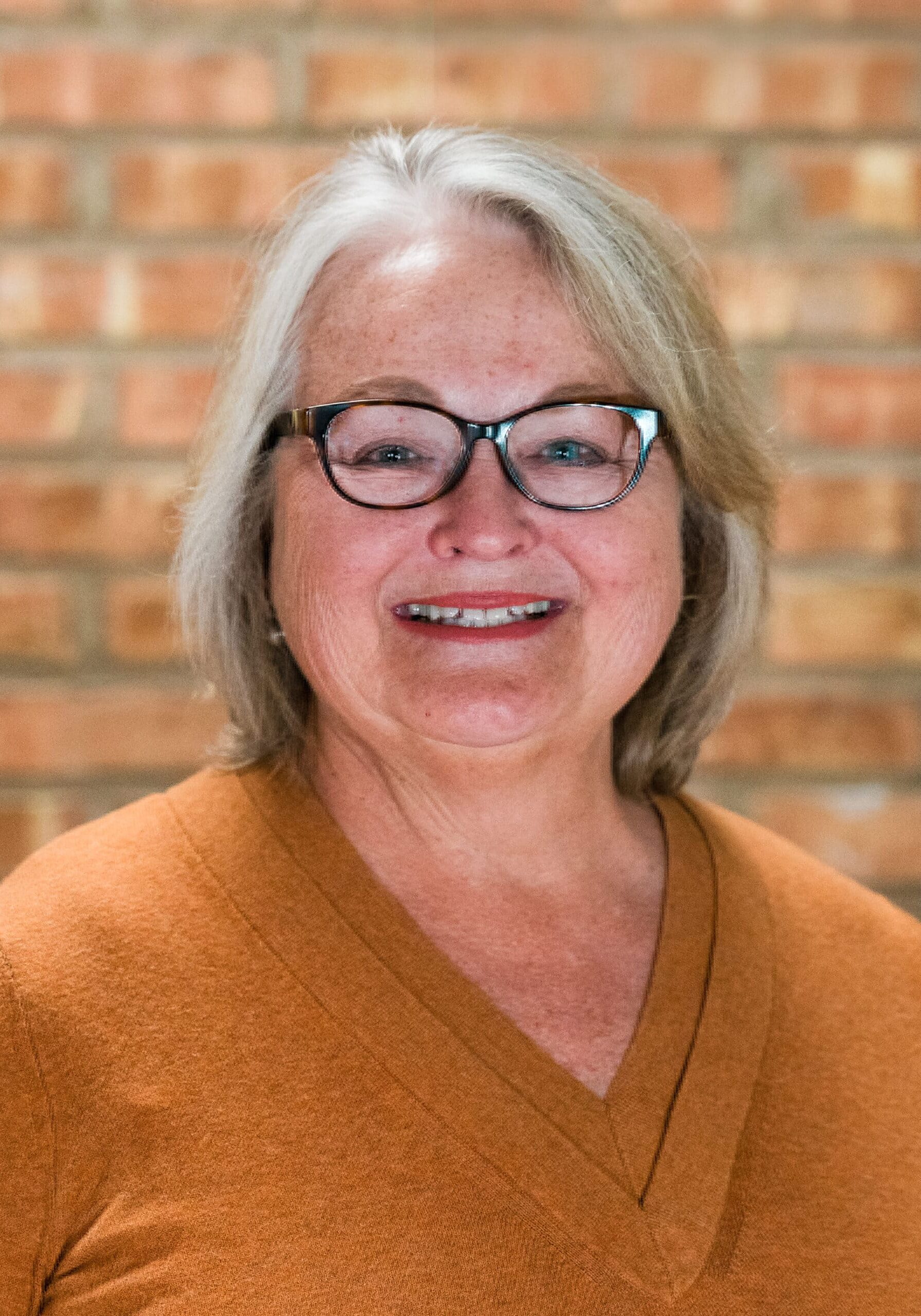 Warm, welcoming woman with glasses at Camp One Step healing retreat.